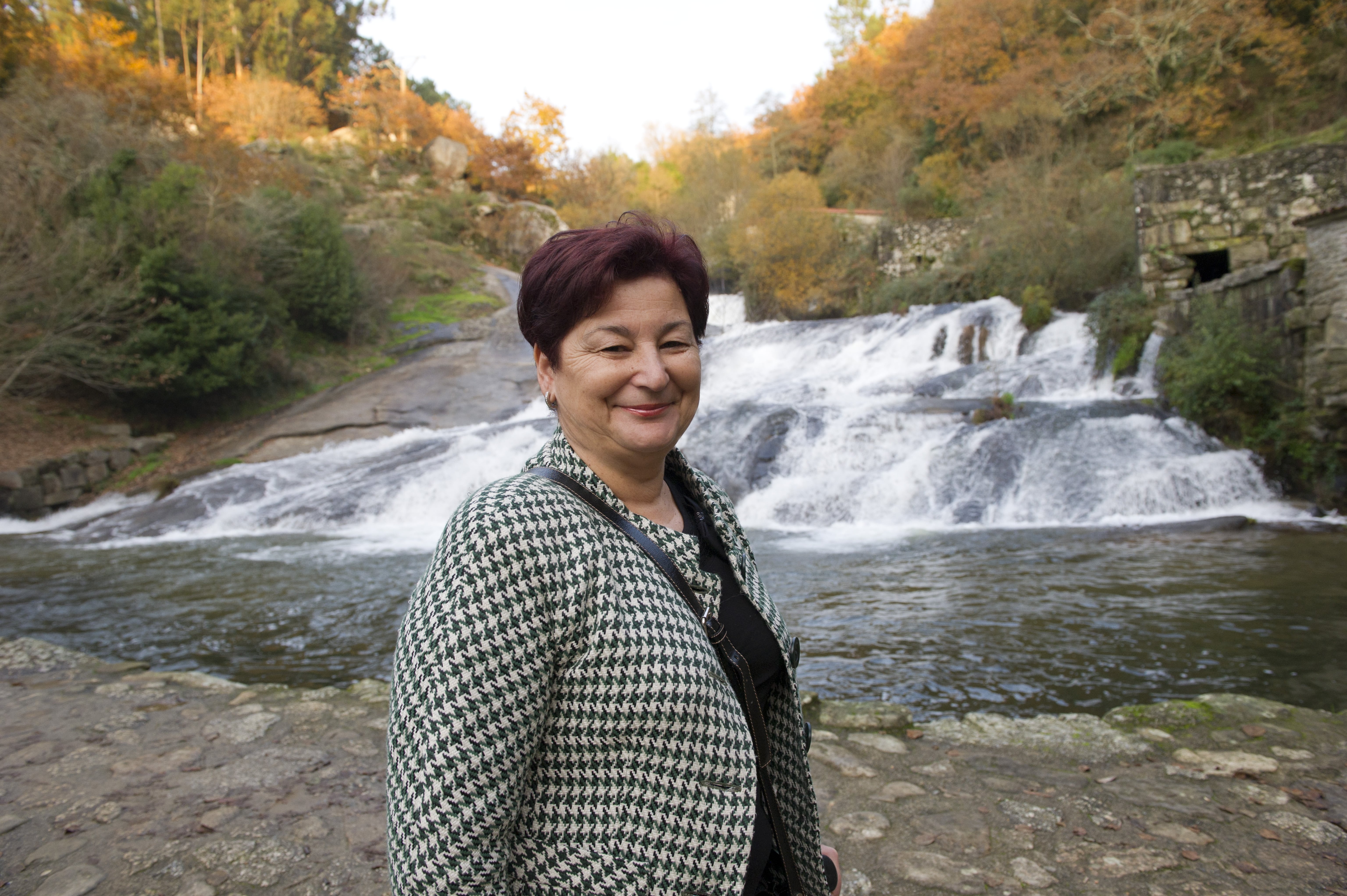 A smiling woman standing in front of a waterfall.